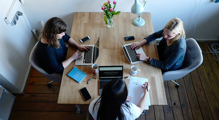 Three business women, working at a shared desk space