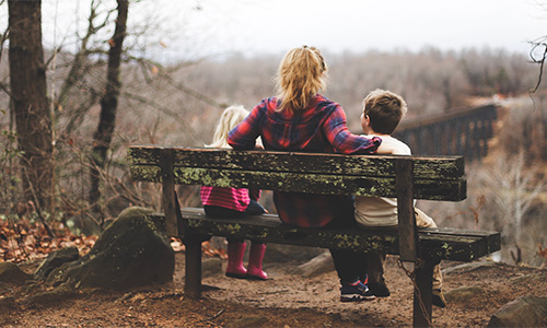 Mum sat on a bench overlooking a valley with her two young children